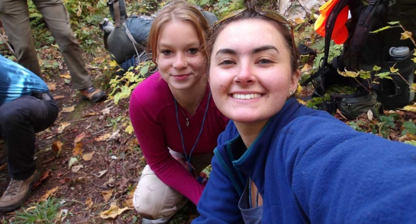 Two people smile for a selfie in a wooded area